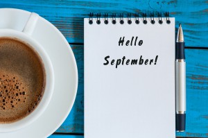 Hello September wrote at paper notepad on blue wooden background with cup of morning coffee. Top view.