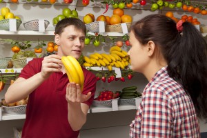 Young woman buys banana. Assistant helping customer at vegetable counter of farm shop
